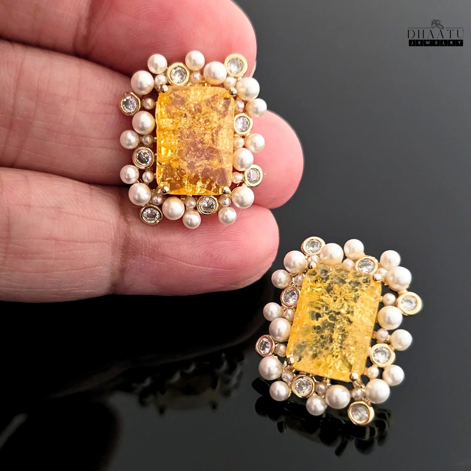 Macro shot of DHAATU JEWELRY earrings held in a hand, showcasing the intricate detail of the citrine, polki stones, and freshwater pearls.