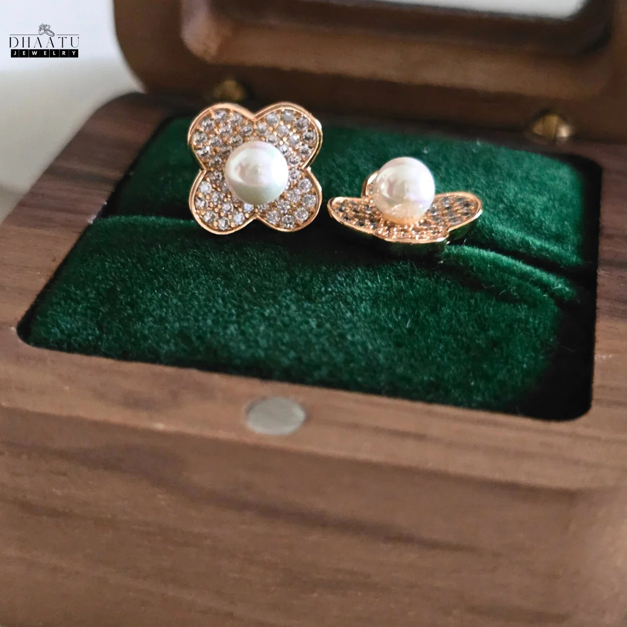 DHAATU JEWELRY gold-plated clover pearl and zircon stud earrings in a wooden box with one earring slightly out, highlighting the pearl and zircon details.

