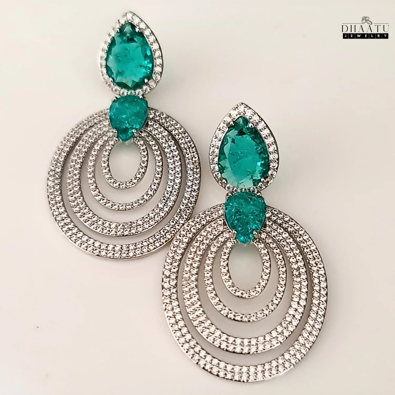 A pair of DHAATU JEWELRY emerald green and pave diamond chandelier earrings displayed on a white background.