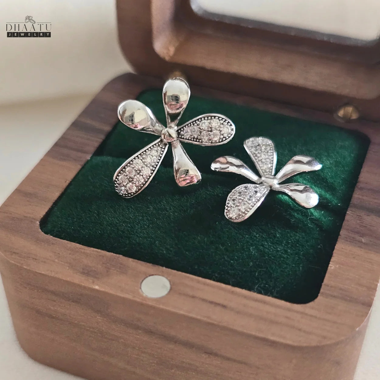 Pair of Dhaatu Jewelry floral stud earrings in a wooden jewelry box with a green velvet interior, viewed from an angle
