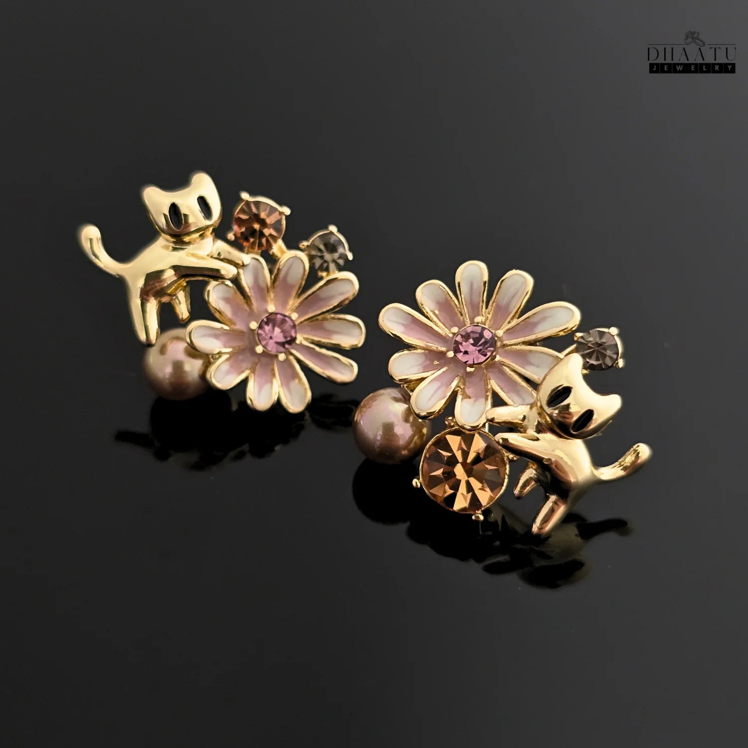 The gold cat and floral earrings on a reflective black surface, creating a striking visual contrast.