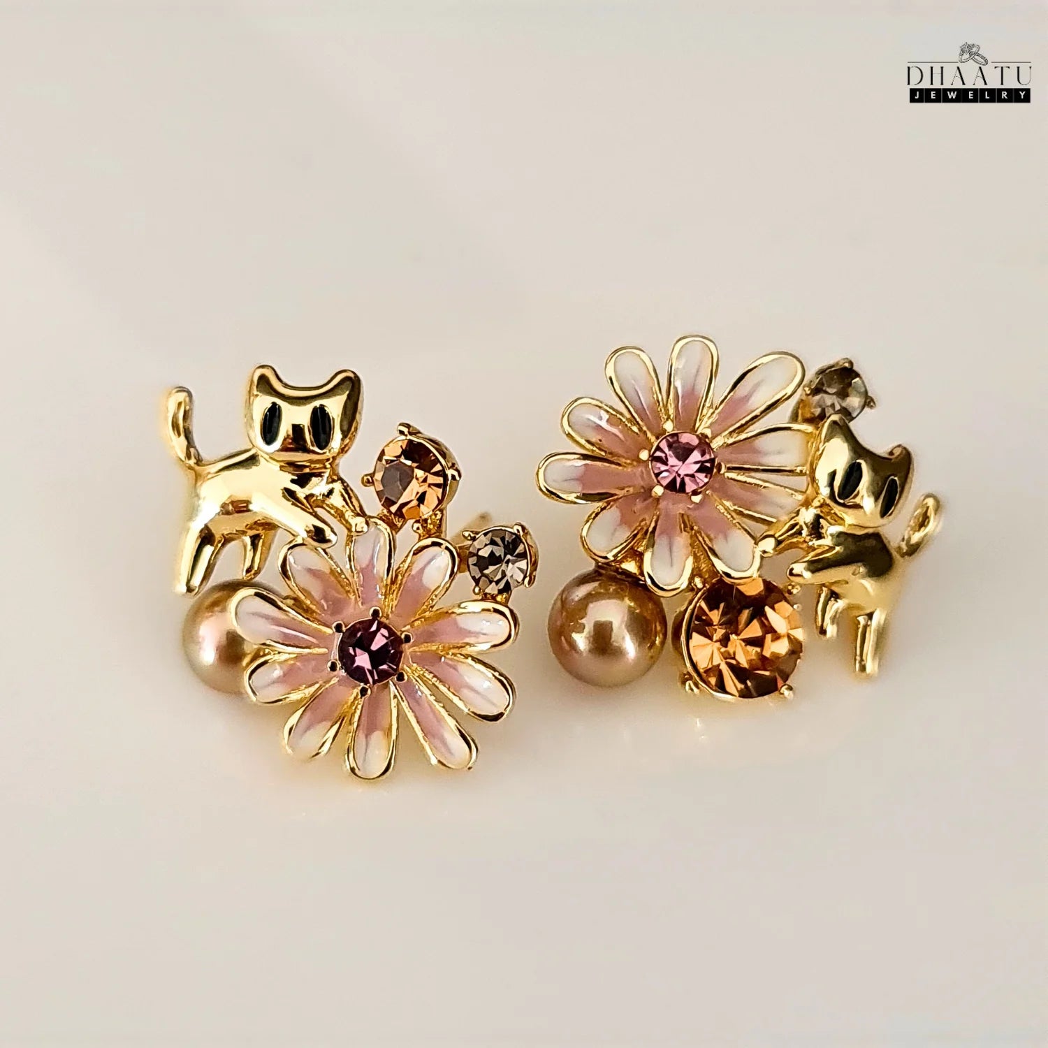 The gold cat and floral earrings displayed on a clean white background, highlighting the contrast of the colors and finishes.