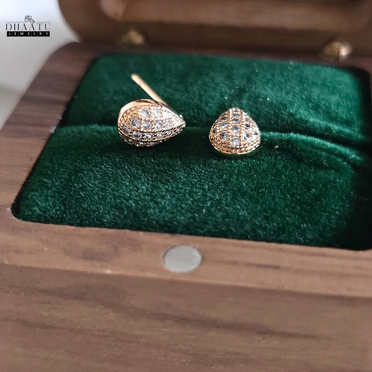 Angled view of Dhaatu Jewelry gold pave teardrop stud earrings in a wooden box with green velvet lining.