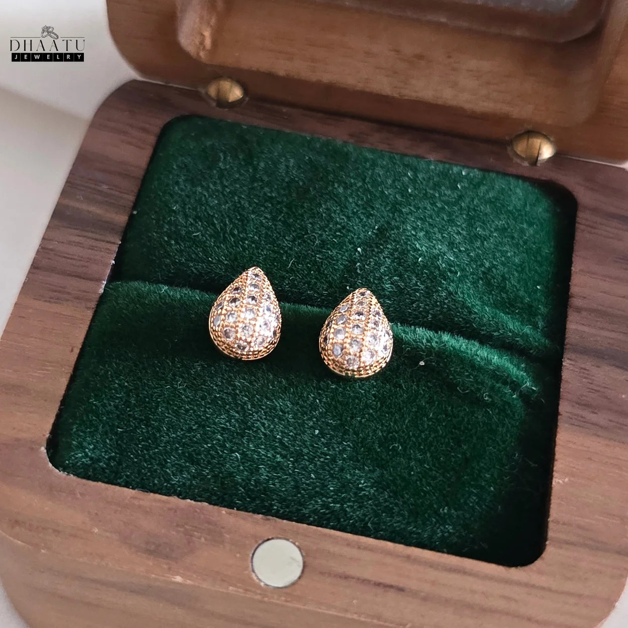 Dhaatu Jewelry gold pave teardrop stud earrings displayed in a dark wooden jewelry box with a green velvet interior