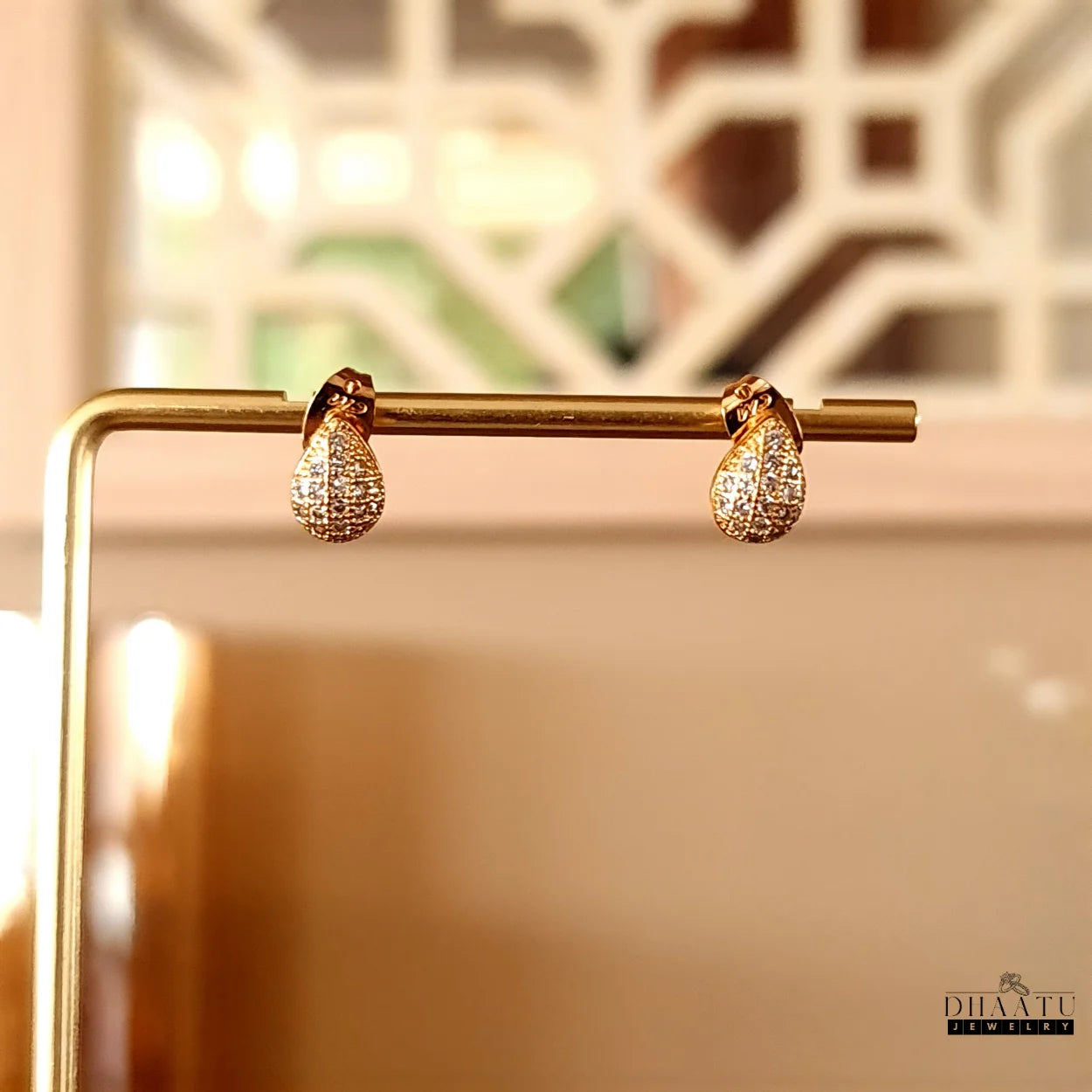 Dhaatu Jewelry gold pave teardrop stud earrings hanging on a golden display bar, showcasing their design