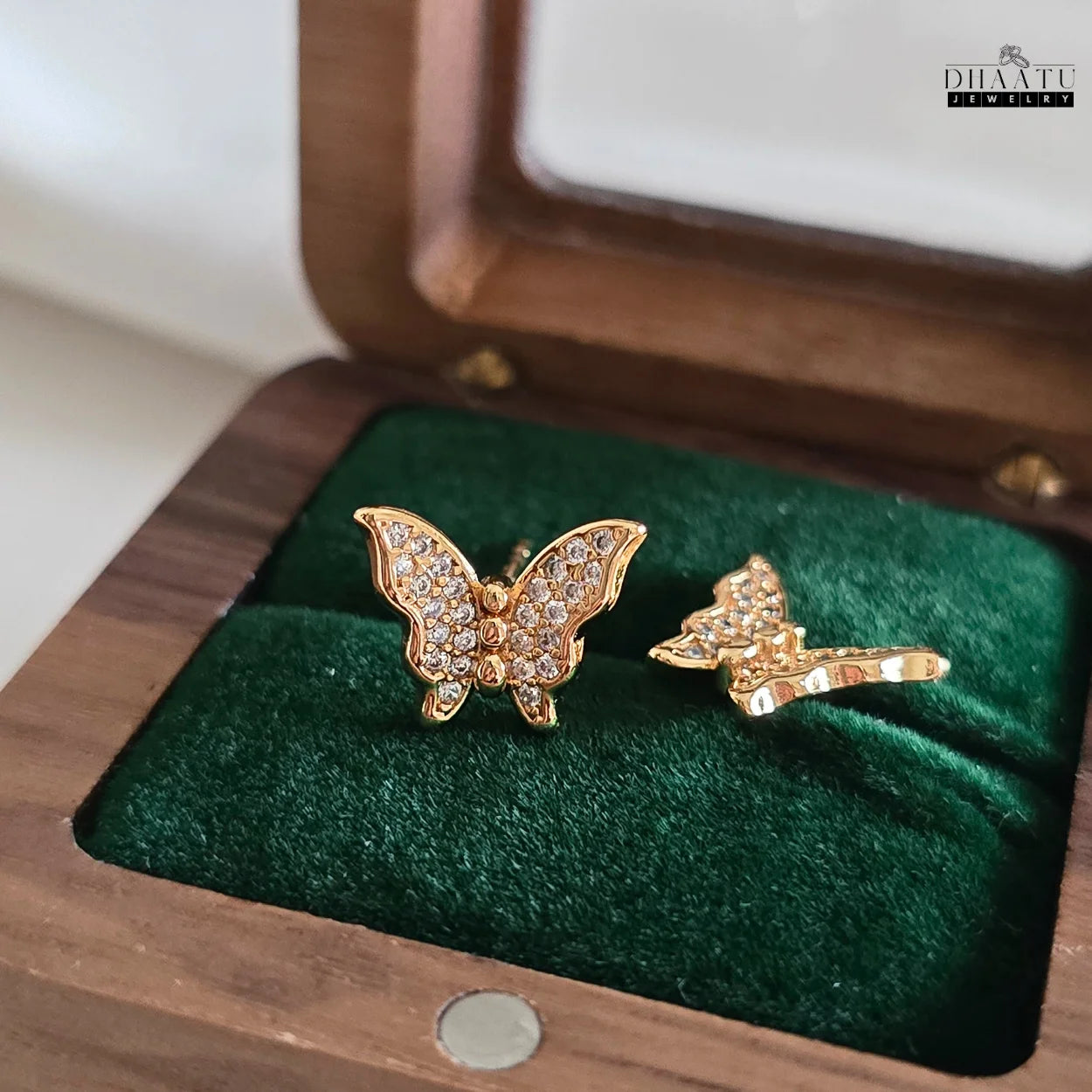 Close-up of a single Dhaatu Jewelry gold-plated butterfly stud earring with cubic zirconia, displayed in a green velvet-lined wooden jewelry box.