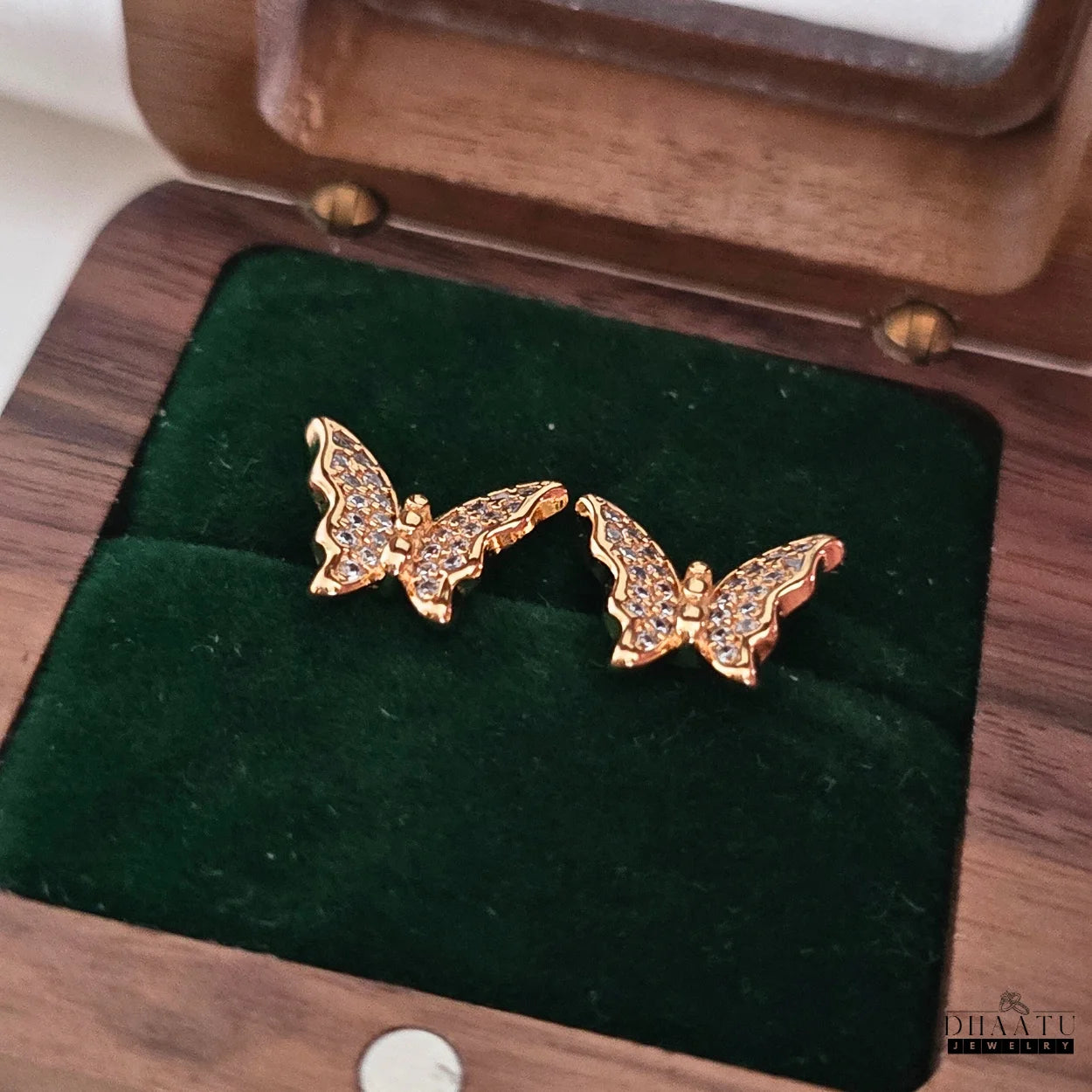 Pair of Dhaatu Jewelry gold-plated butterfly stud earrings with cubic zirconia, neatly placed inside a dark green velvet-lined wooden jewelry box