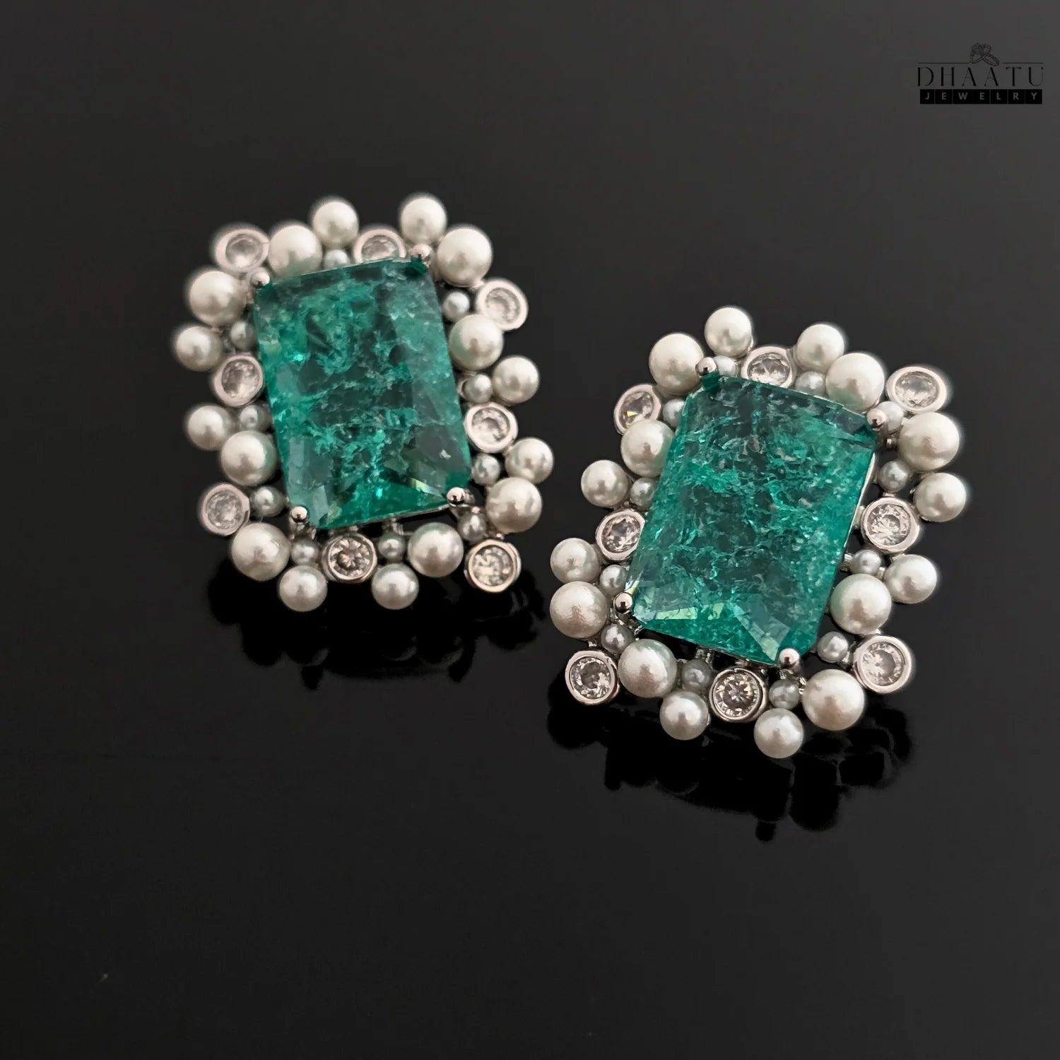 Pair of earrings with green gemstones and silver accents on a black background