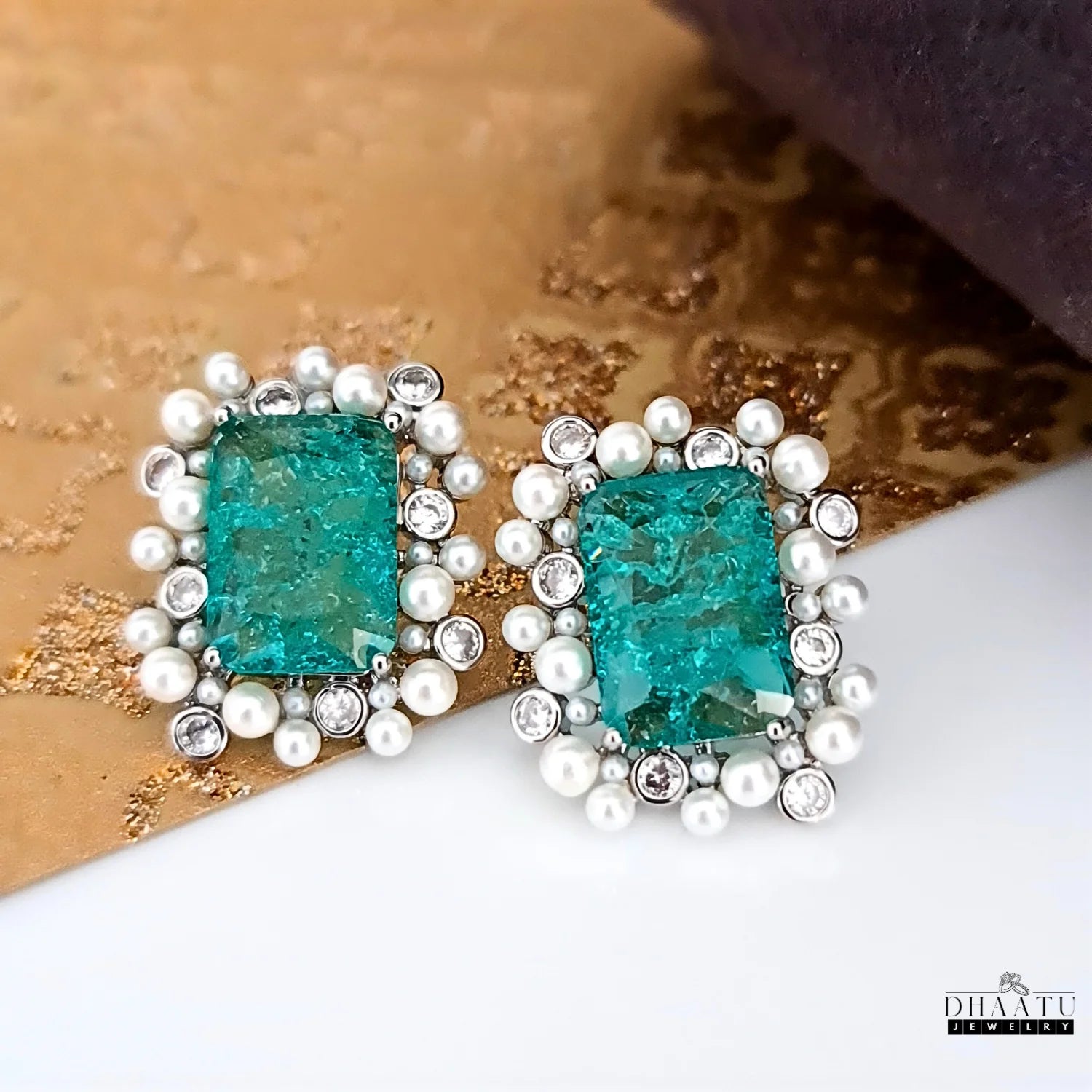 Teal gemstone earrings with pearl accents on a textured surface