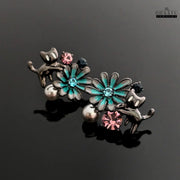 The gunmetal cat and floral earrings placed on a reflective black surface, emphasizing the shine and intricate details.