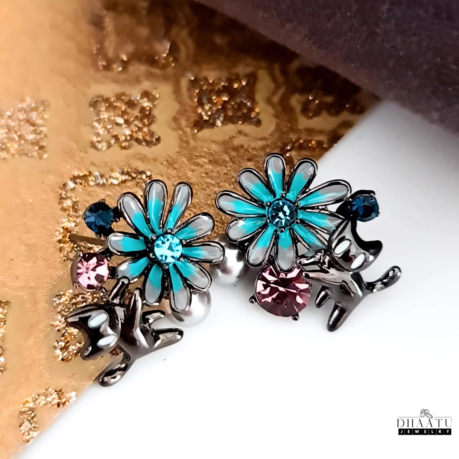 A close-up shot of the gunmetal cat and floral earrings, featuring a turquoise enamel flower and various colorful crystals.