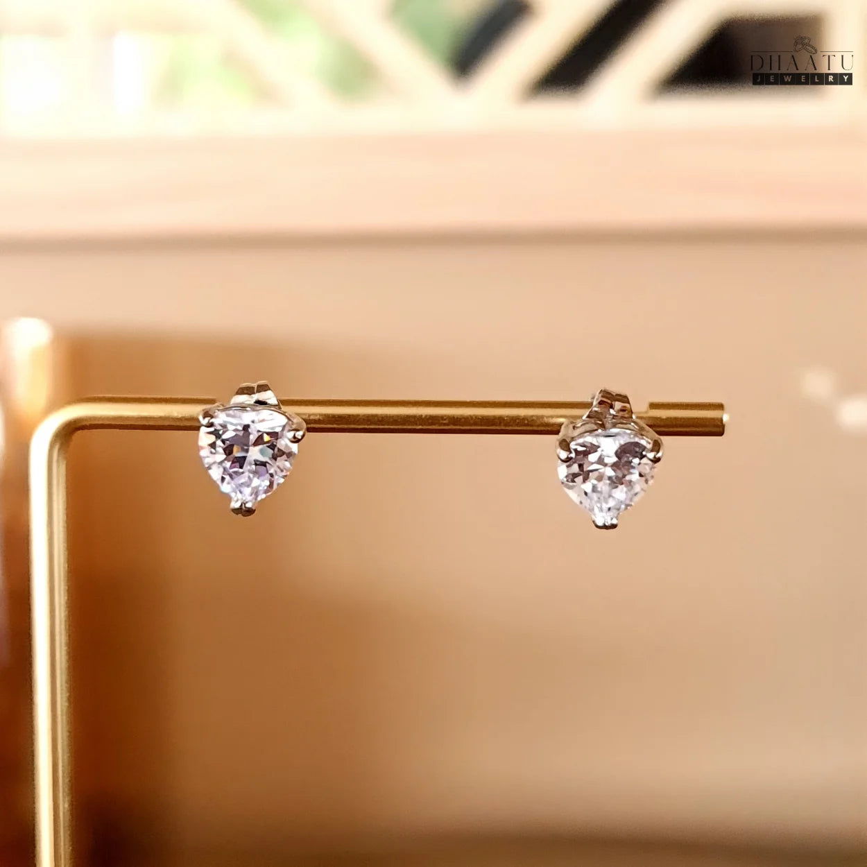 Sparkling heart-shaped AD stud earrings from Dhaatu Jewelry elegantly displayed on a golden jewelry stand.
