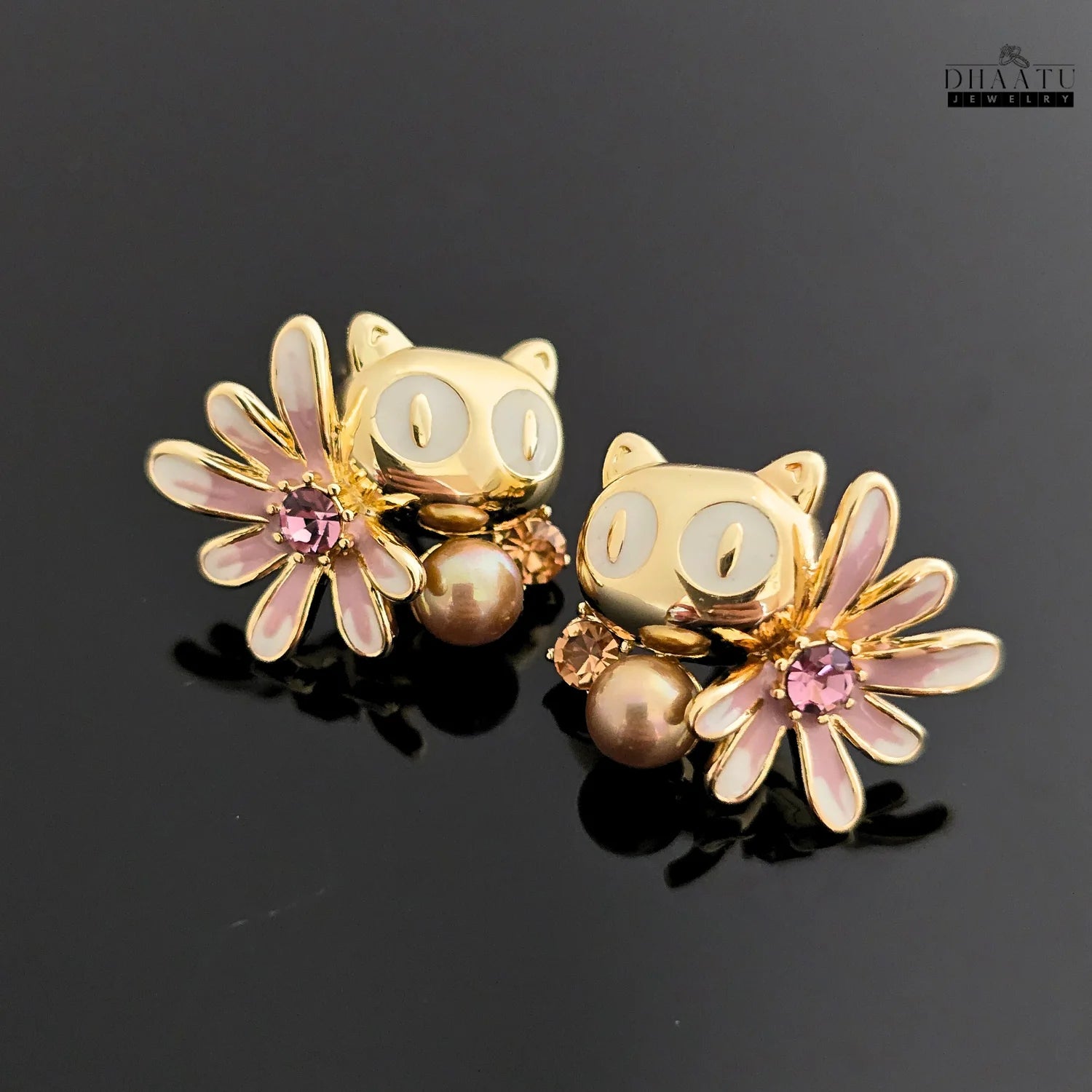 Pair of Dhaatu Jewelry owl stud earrings with white eyes and mocha pearls on a reflective black background.