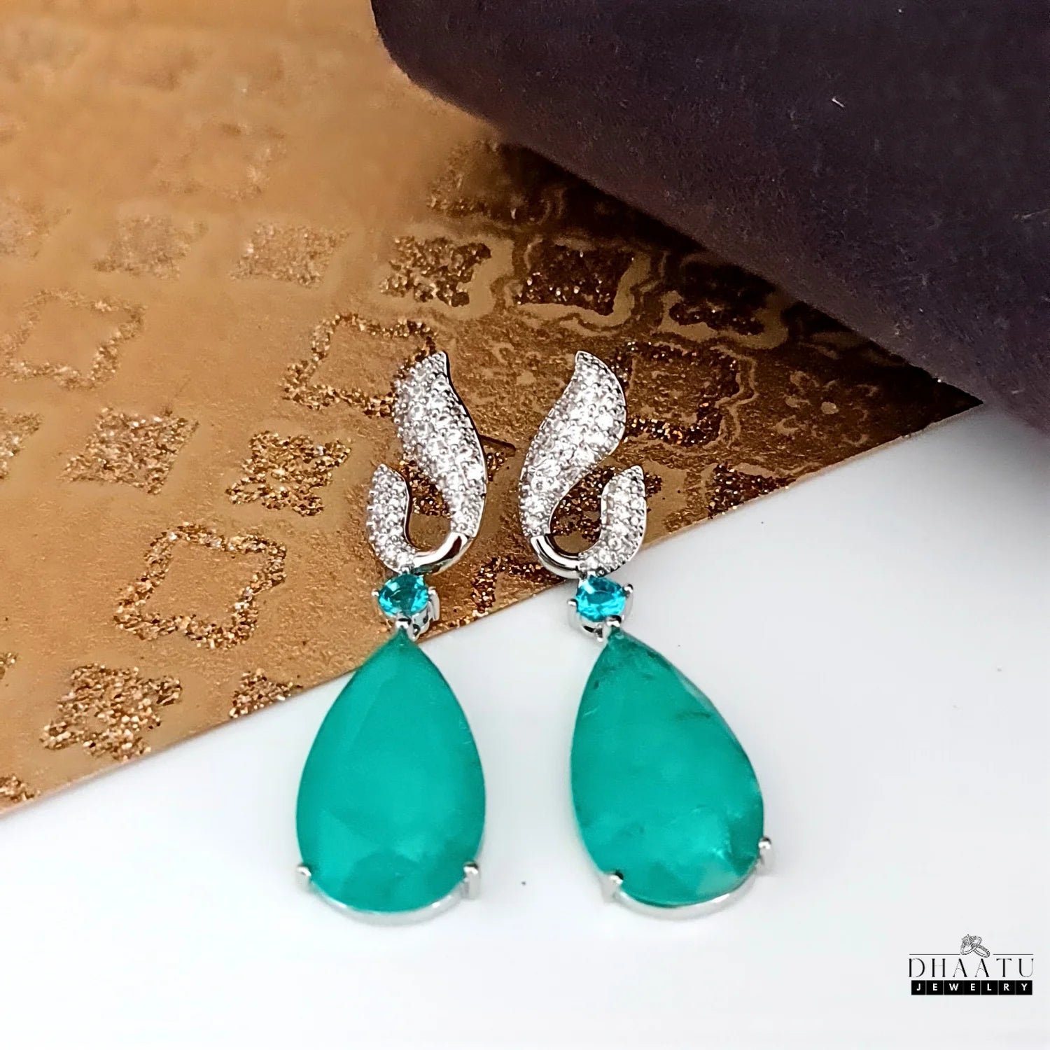 Dhaatu Jewelry green Paraiba stone dangle earrings with zircon detailing and white rhodium plating on a clean white surface.

