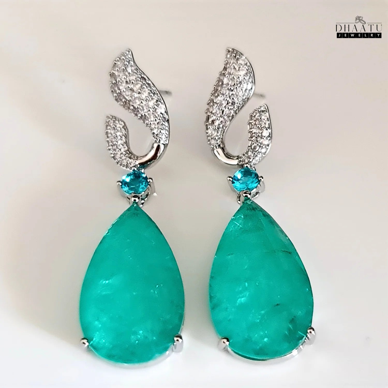 Dhaatu Jewelry green Paraiba stone dangle earrings with zircon detailing and white rhodium plating on a clean white surface.

