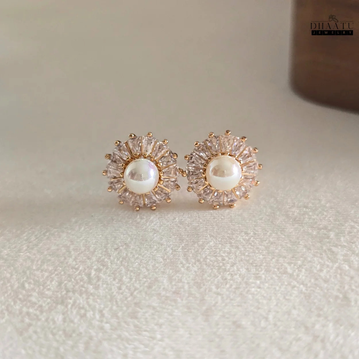 Pair of DHAATU JEWELRY Pearl and Cubic Zirconia Sunburst Stud Earrings resting on a textured white fabric, showing overall design.

