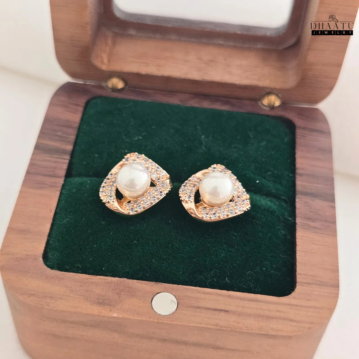 Pair of Dhaatu Jewelry pearl and zircon stud earrings in a dark wooden jewelry box with green velvet lining