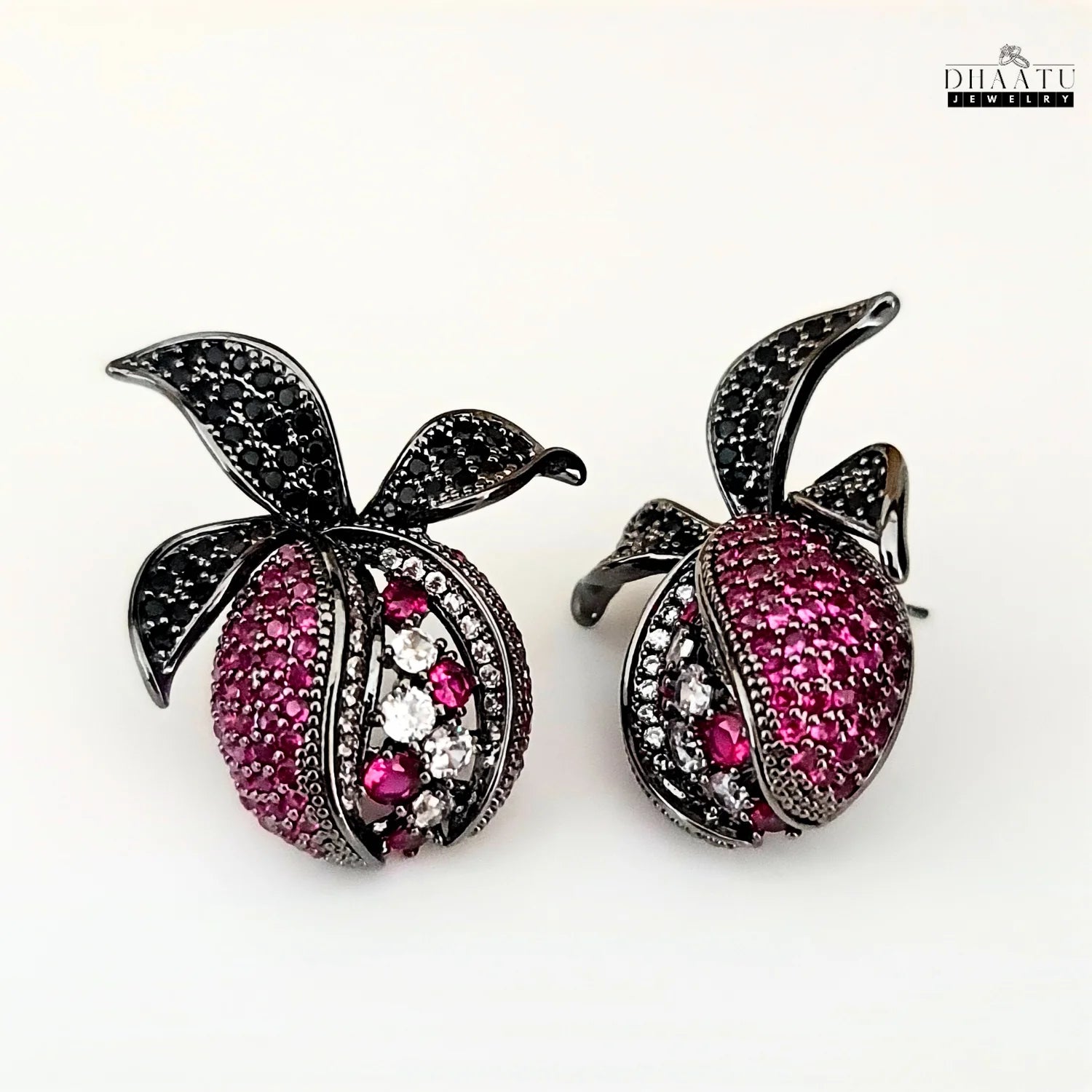 Pomegranate-themed stud earrings from DHAATU JEWELRY with a black rhodium polish and sparkling pink, white, and black zircons on a clean white background.