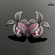 Pomegranate-inspired stud earrings with black rhodium finish, featuring pink, white, and black zircon stones on a black reflective background.