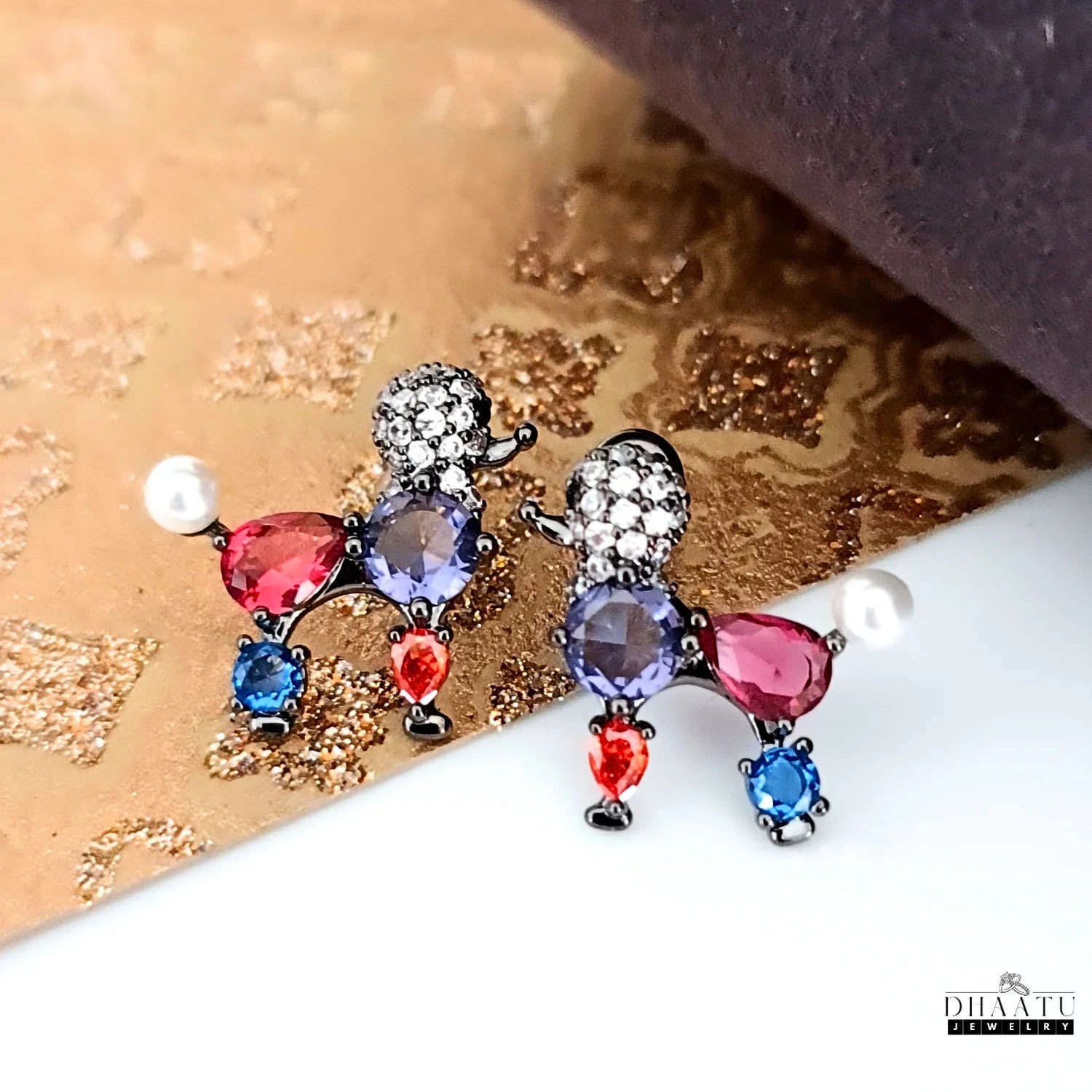 Close-up of multicolor crystal poodle earrings on a shiny gold and brown fabric background.