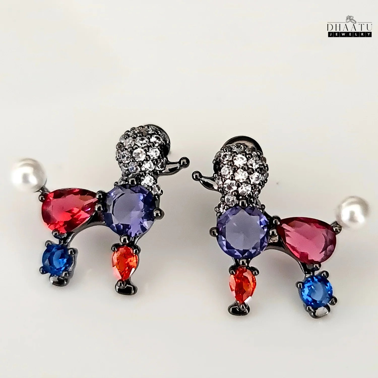 A pair of multicolor poodle stud earrings with crystals and a faux pearl on a white background.