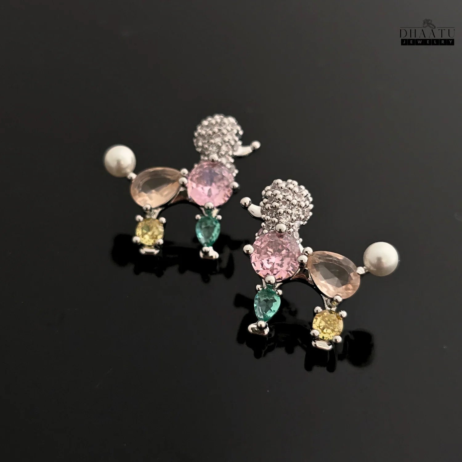 A pair of pastel-colored poodle earrings with faux pearls and crystals on a black surface.