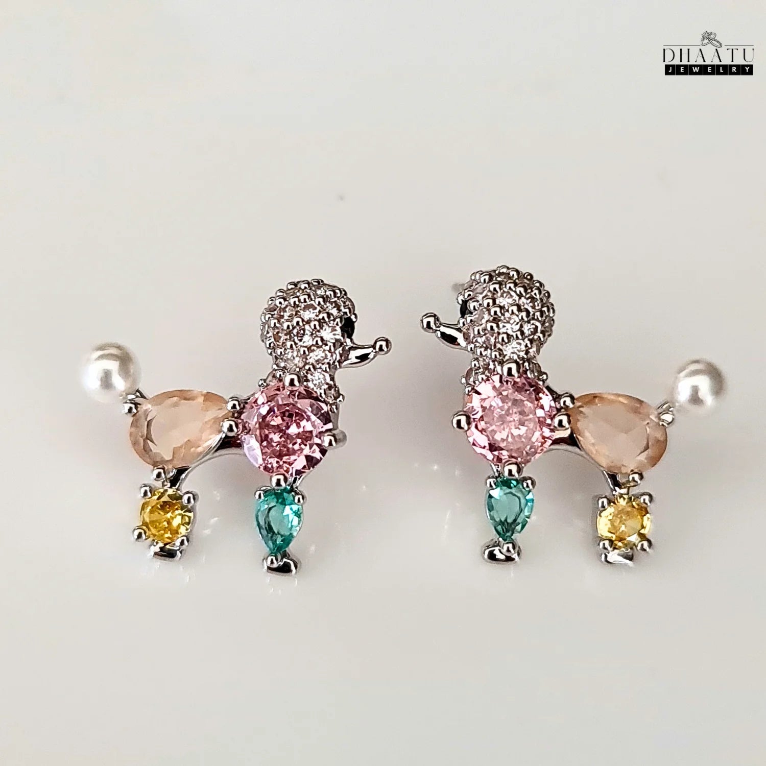 A pair of pastel-colored poodle earrings with faux pearls and crystals on a clean white background.