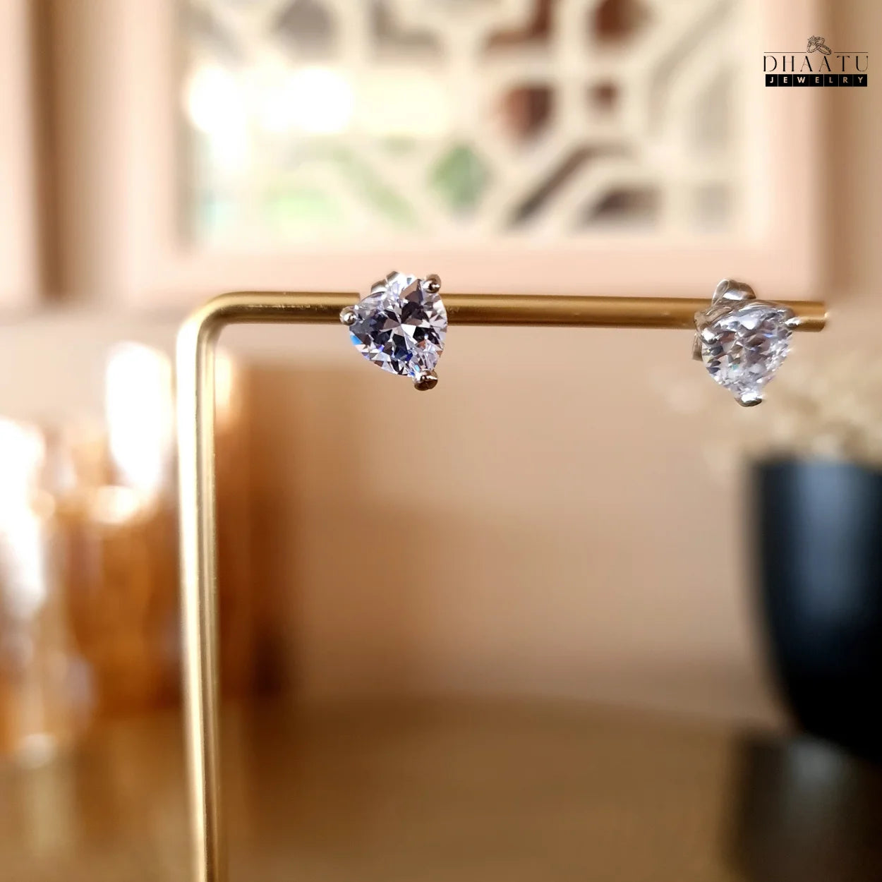 Rose gold finish heart-shaped American Diamond stud earrings from Dhaatu Jewelry, beautifully presented on a golden jewelry display stand.