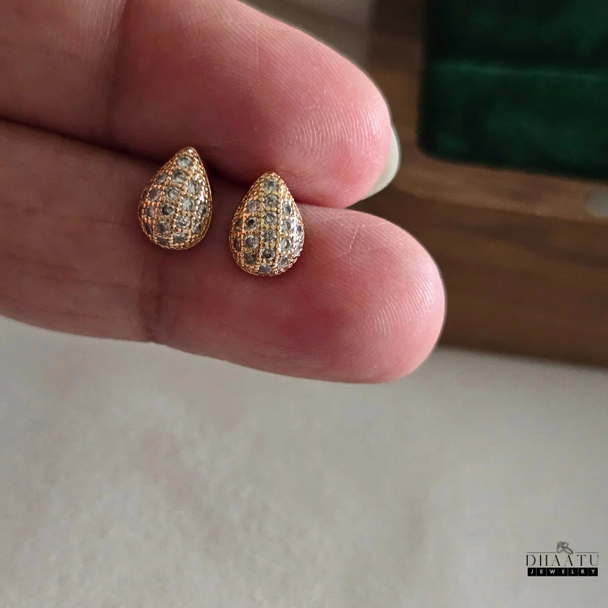 Dhaatu Jewelry rose gold pave teardrop stud earrings held delicately on a person's hand, showing their size and shimmer.