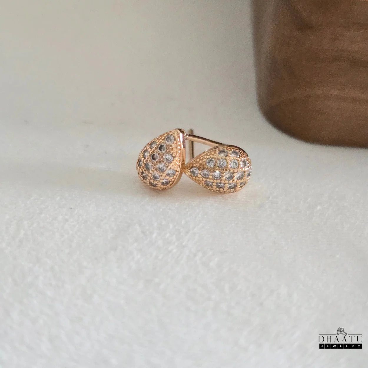Close-up of Dhaatu Jewelry rose gold pave teardrop stud earrings on a white surface, highlighting the warm tone