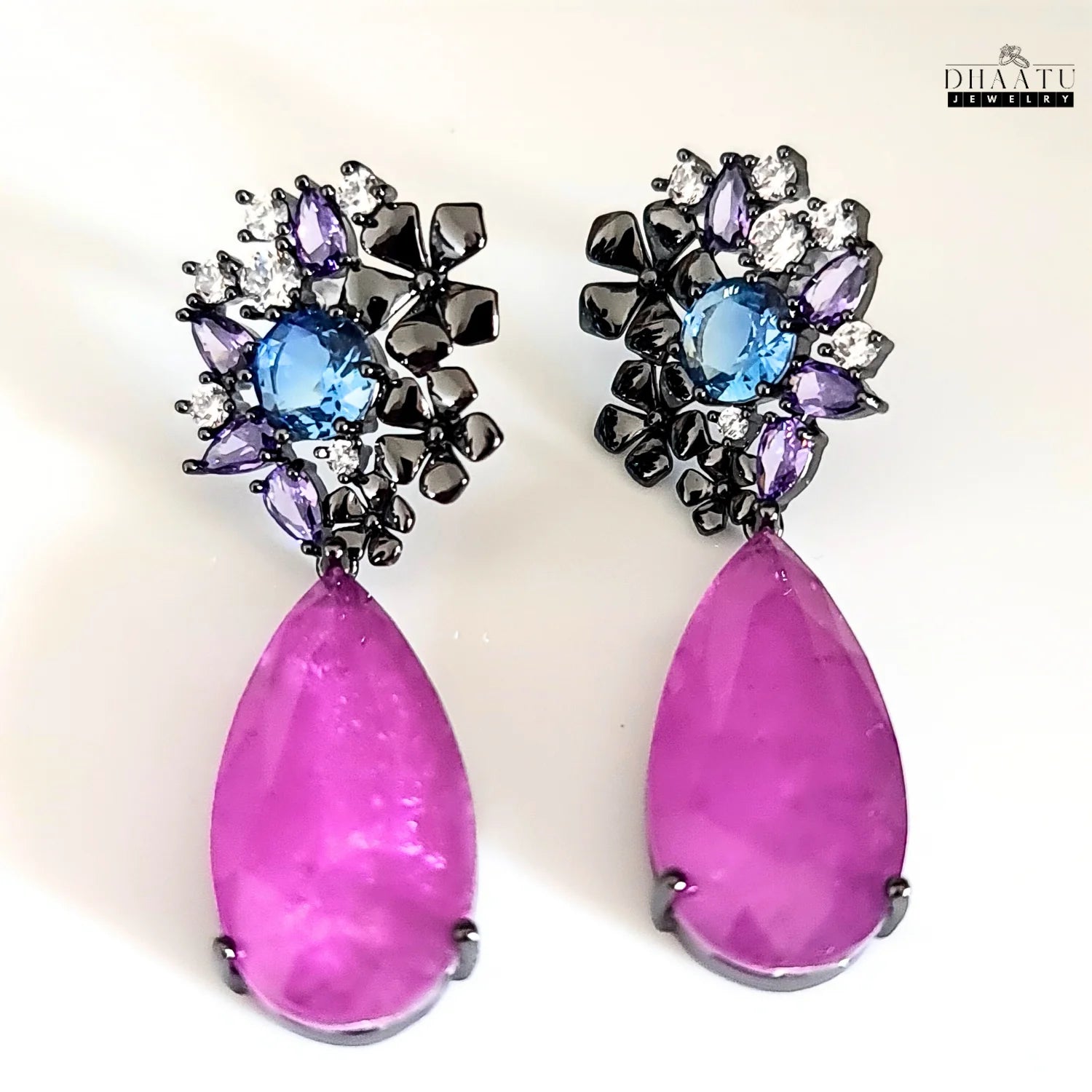 DHAATU JEWELRY drop earrings featuring floral stud with blue and purple stones and a violet teardrop, on a white background.