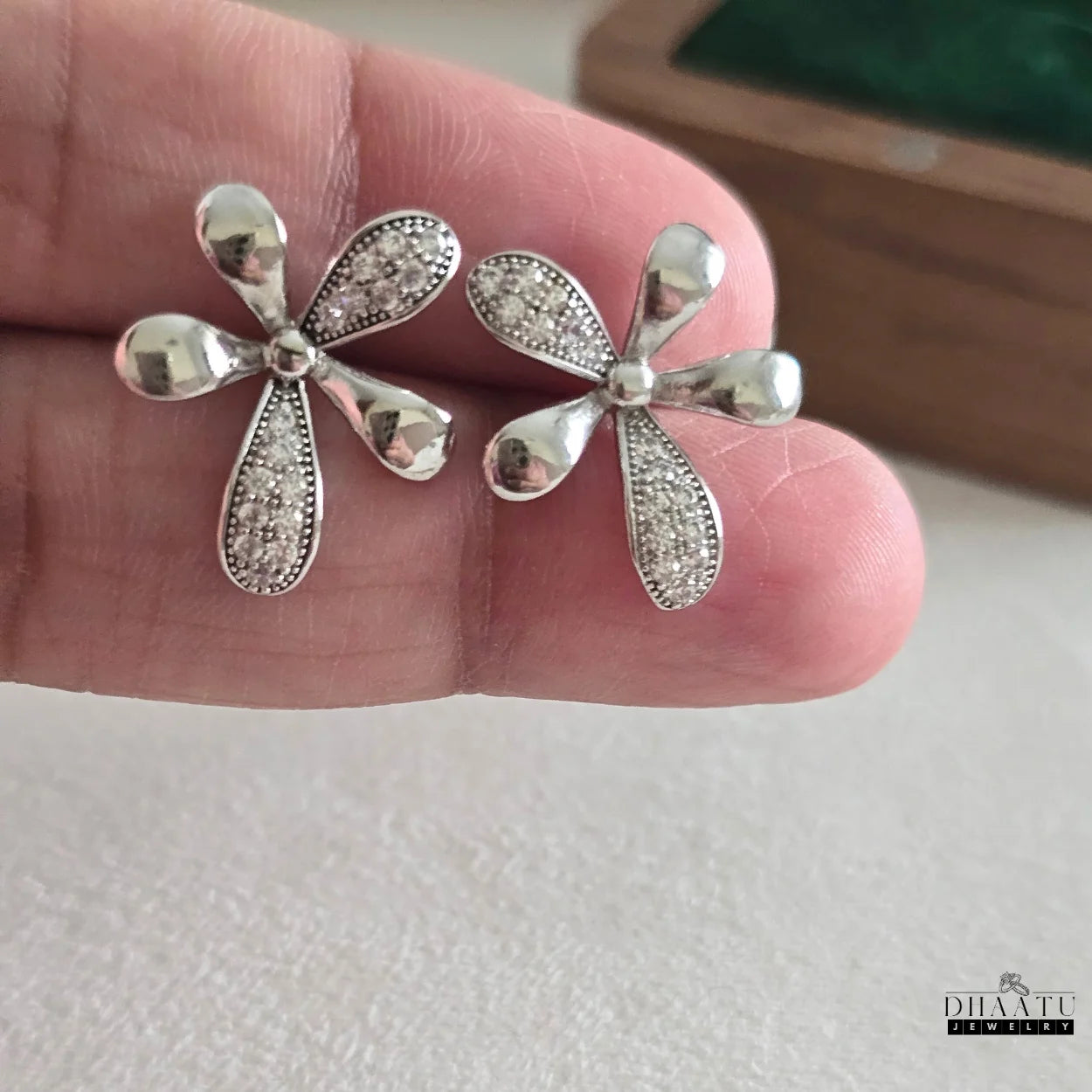 Closeup of Dhaatu Jewelry silver-plated floral stud earrings with sparkling cubic zirconia and polished petals, held by hand