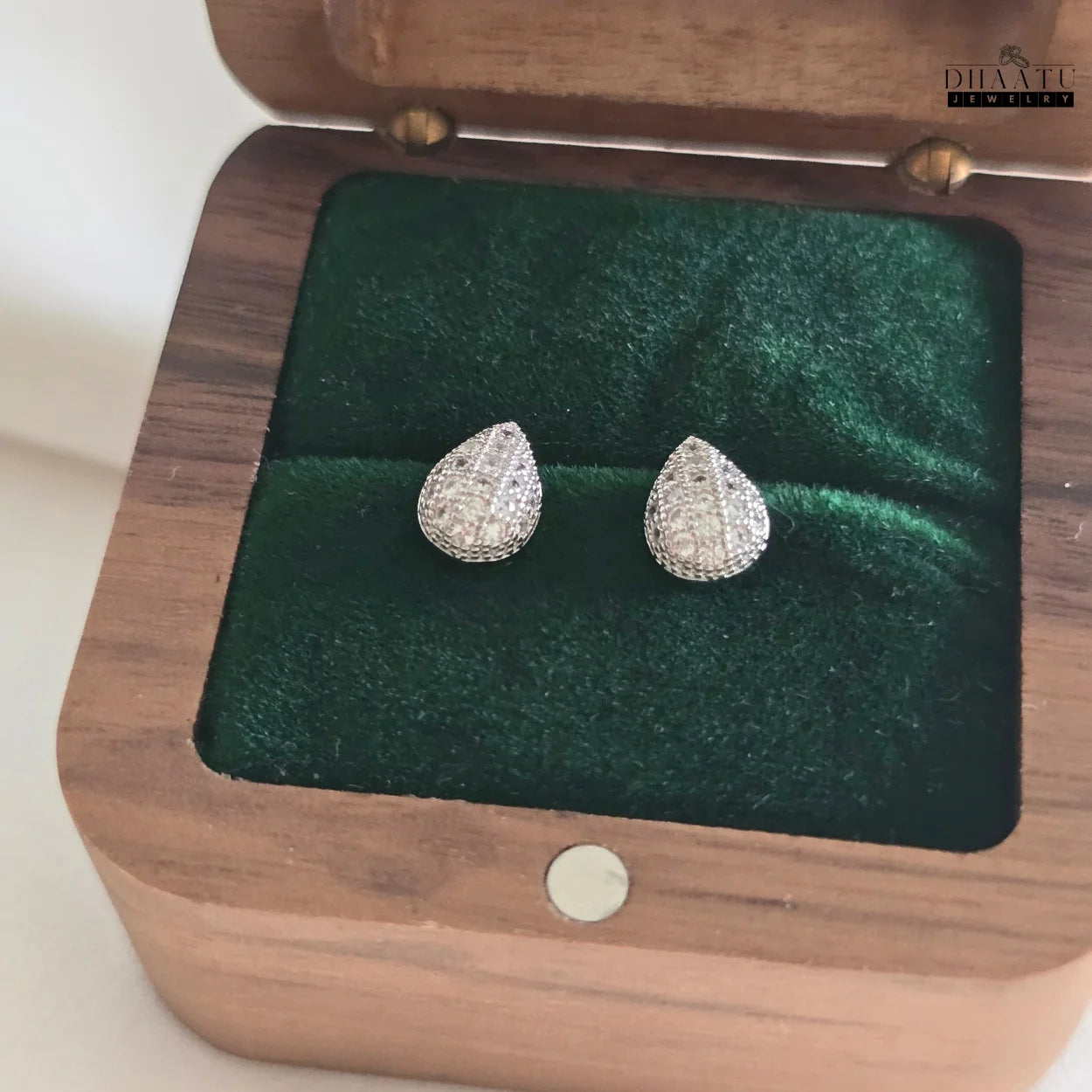 Dhaatu Jewelry silver pave teardrop stud earrings neatly placed inside a wooden jewelry box with a dark green velvet interior.