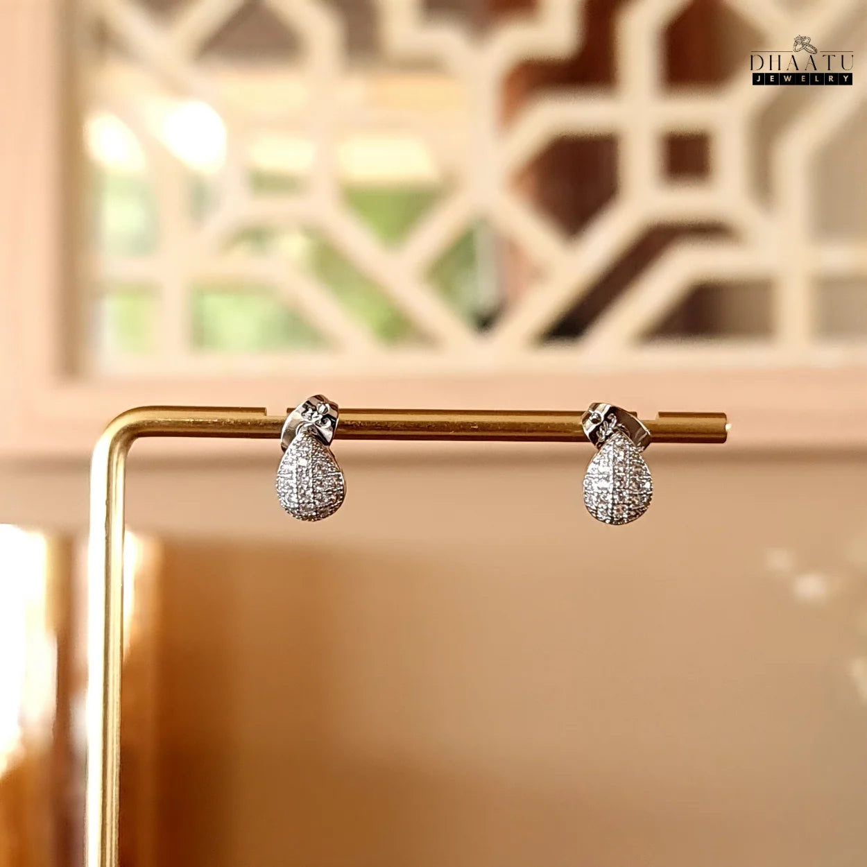 Dhaatu Jewelry silver pave teardrop stud earrings displayed on a golden stand, highlighting their elegant shape.
