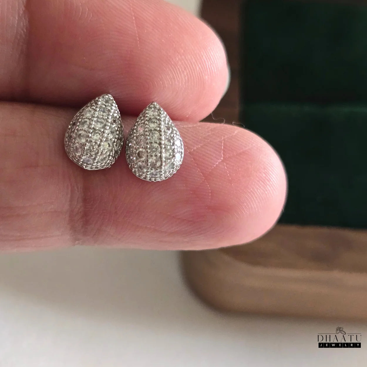 Close-up of Dhaatu Jewelry silver pave teardrop stud earrings held on a finger, showcasing intricate stone detailing.