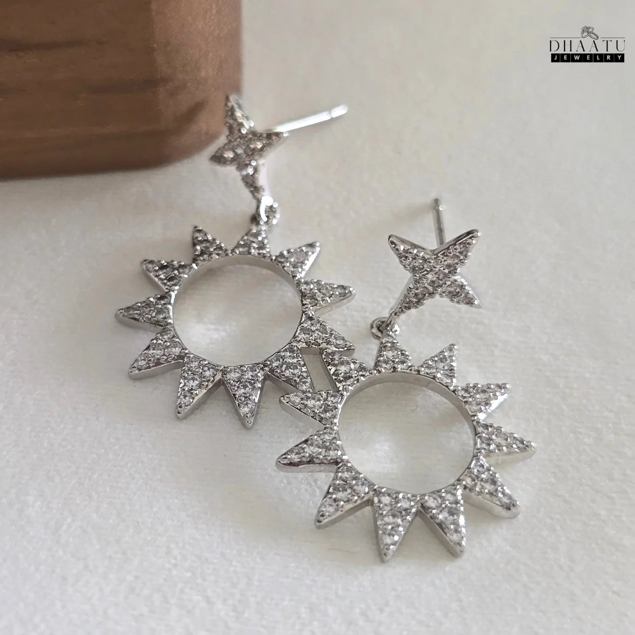 Detailed shot of Dhaatu Jewelry silver-plated star and sunburst dangle earrings with clear zircon stones on a white background.