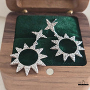 Pair of Dhaatu Jewelry silver-plated star and sunburst earrings with zircon stones presented in a wooden jewelry box.