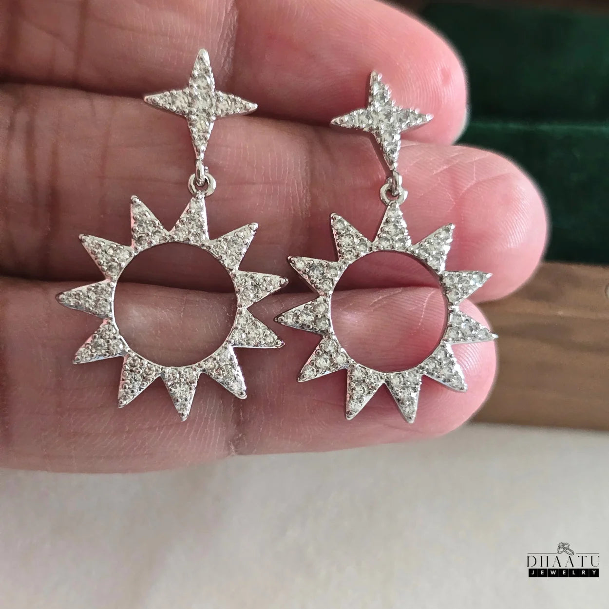 Handheld view of Dhaatu Jewelry silver-plated star and sunburst earrings, highlighting the brilliant zircon stones and design.