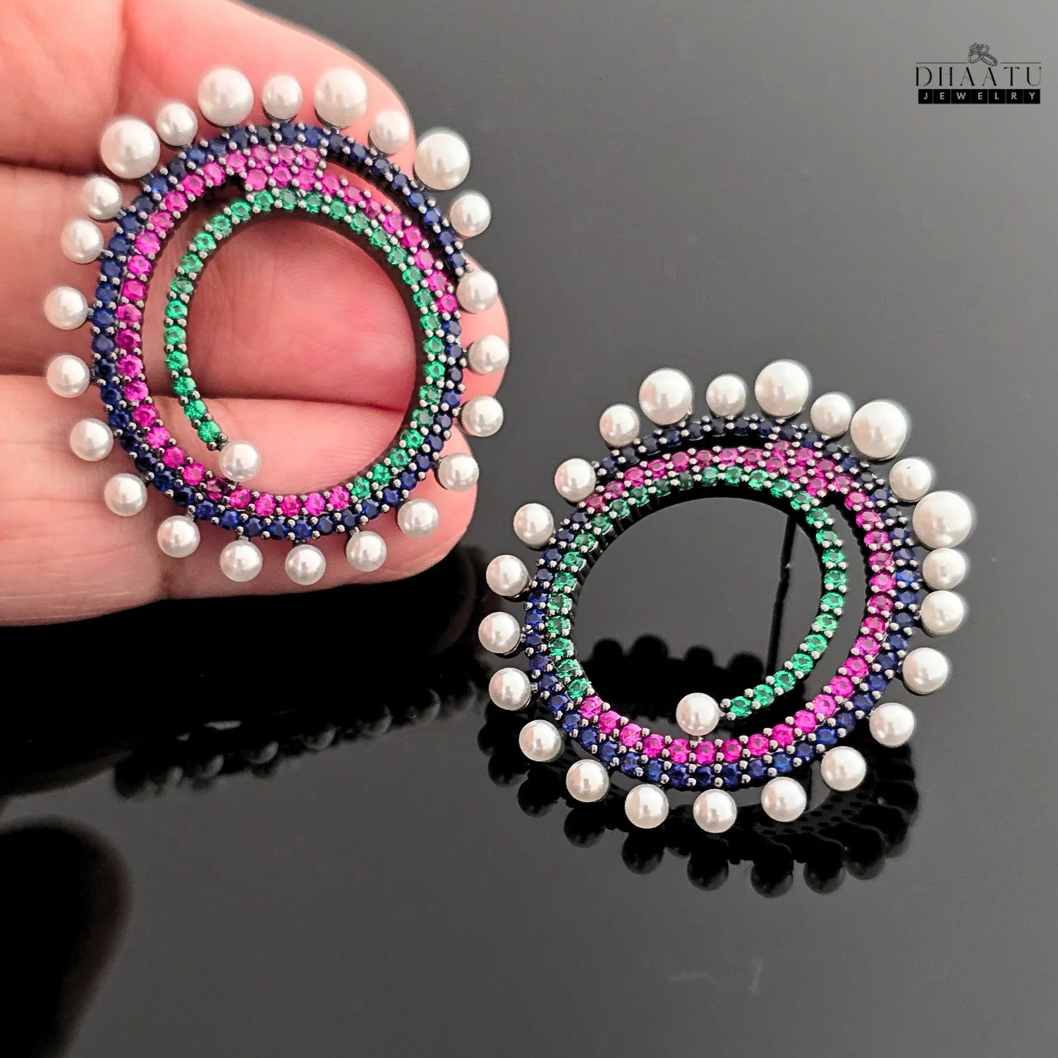 Close-up shot of a pair of Dhaatu Jewelry stud earrings, highlighting the intricate spiral design with multi-color gemstones and a white pearl border.