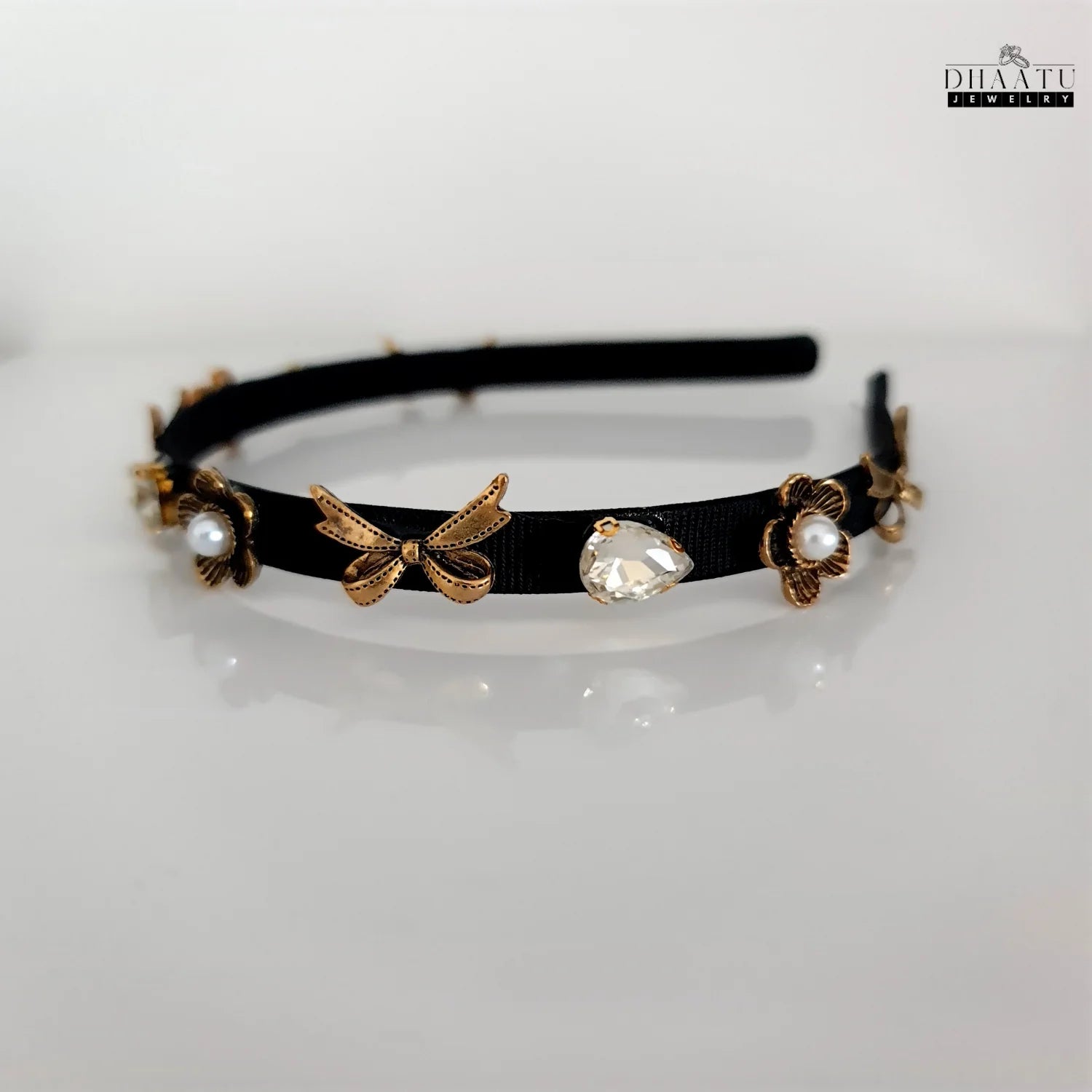 Side view of Dhaatu Jewelry Western-style black hairband with gold bows and flower embellishments against a white background