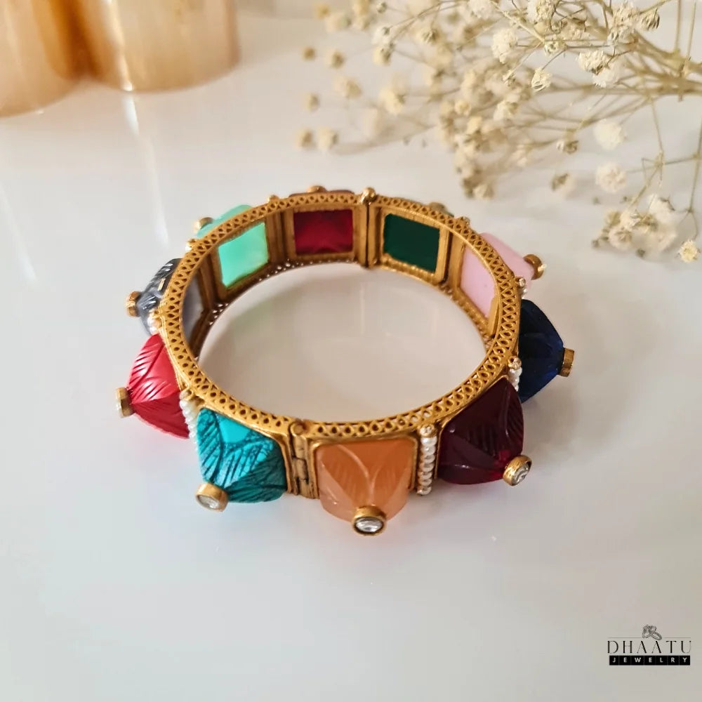 Overhead view of the multicolor carved stone and pearl kada bracelet on a white surface, displaying all the colorful carved stones and the full circular design.

