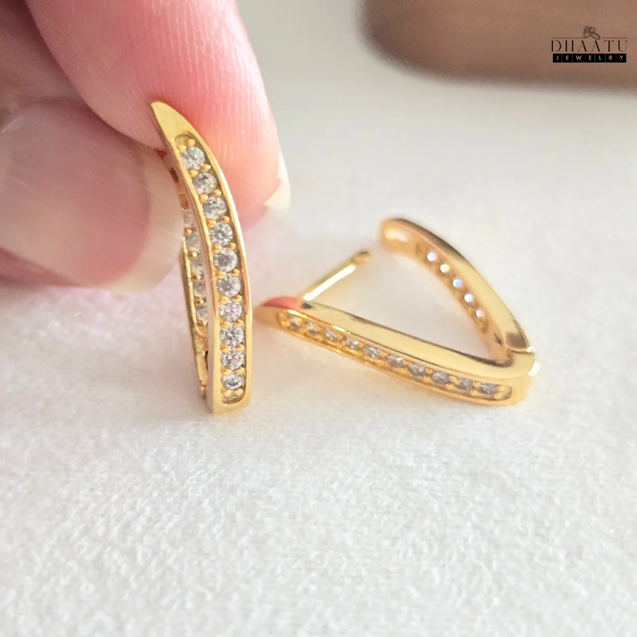 Hand holding one of the Dhaatu gold plated zirconia hoop earrings, showing the intricate details and size