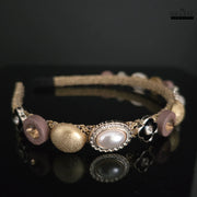 Elegant gold and pearl beaded headband featuring textured gold beads, faux pearls in ornate settings, and black flower accents on a dark background