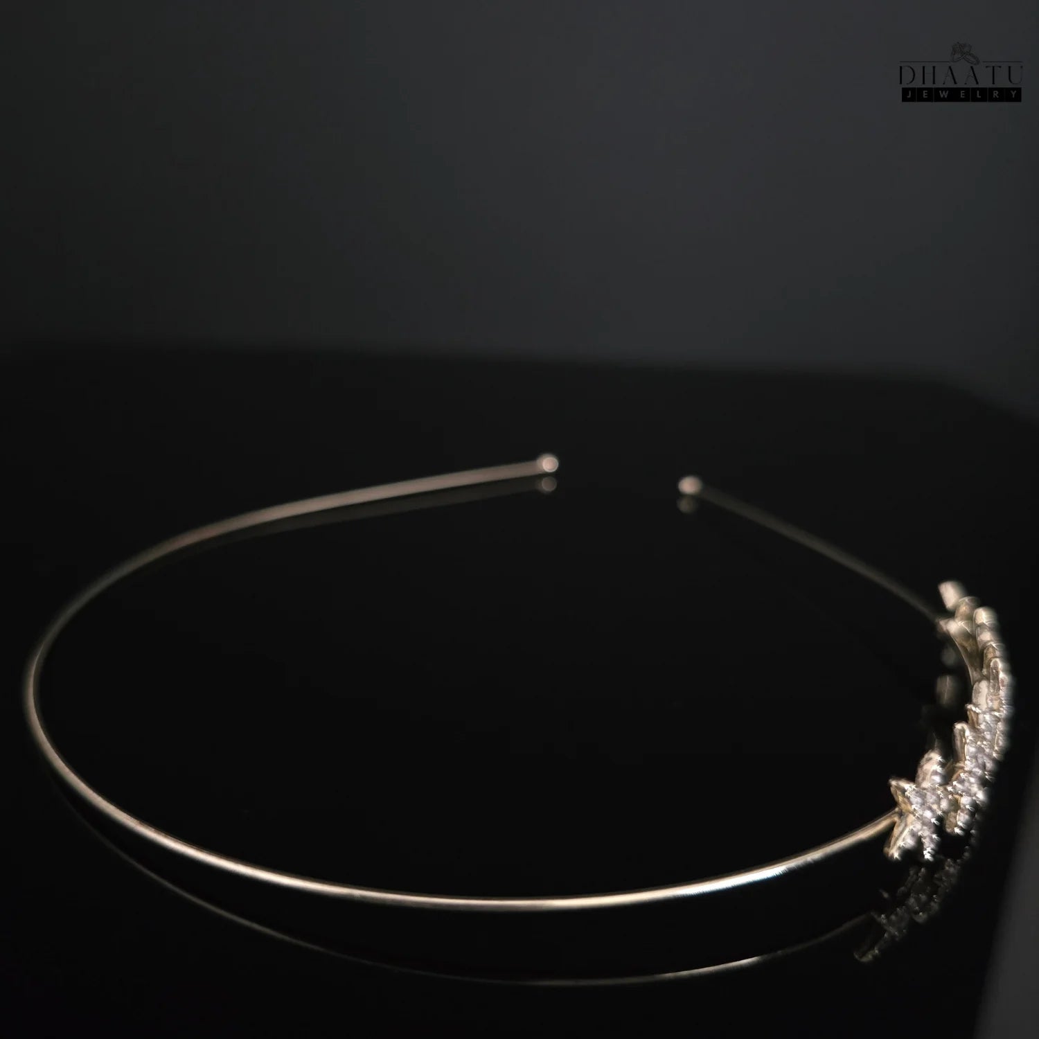 Side view of elegant gold-tone headband with starburst zirconia design, reflecting on a dark surface