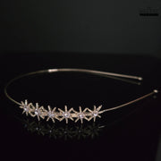 Elegant gold-toned hairband with starburst zirconia embellishments, photographed on a dark reflective surface, emphasizing its sparkle