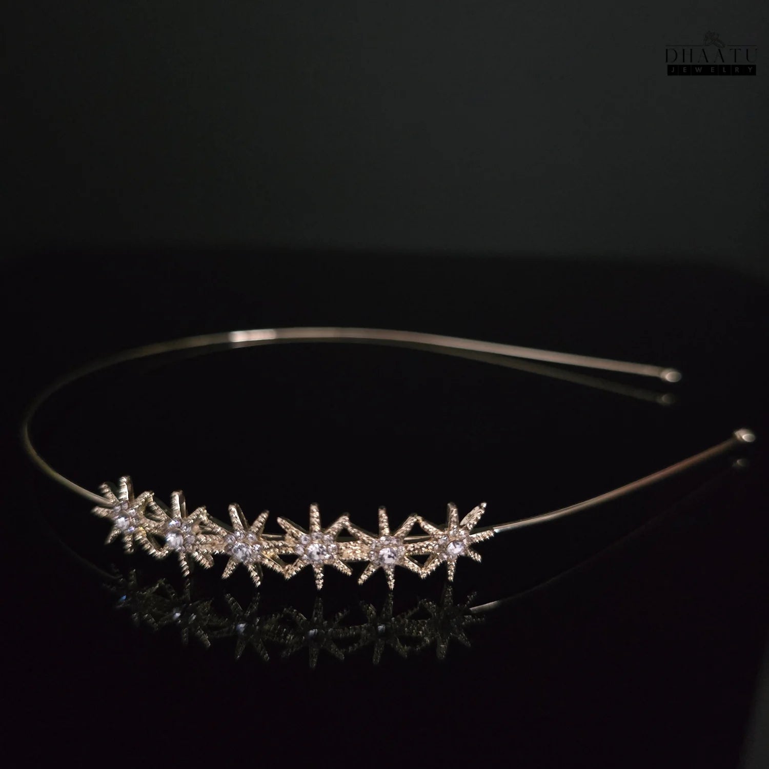 Elegant gold-toned hairband with starburst zirconia embellishments, photographed on a dark reflective surface, emphasizing its sparkle