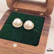 Pearl earrings with rose gold accents on a green cushion inside an open wooden jewelry box.