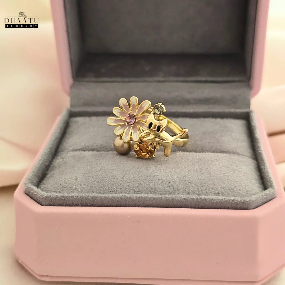 The DHAATU JEWELRY gold-toned cat and floral ring resting inside a pink and grey jewelry box, emphasizing its gift-ready presentation.