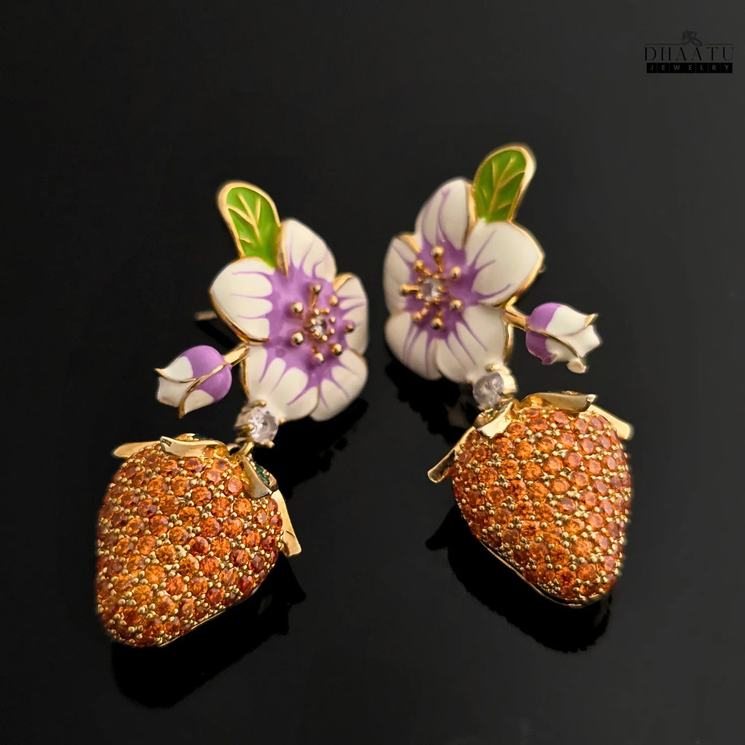 Pair of gold-plated drop earrings with white and purple enamel flowers and orange CZ strawberry charms, shown on a black background.