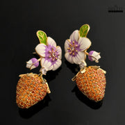 Pair of gold-plated drop earrings with white and purple enamel flowers and orange CZ strawberry charms, shown on a black background.